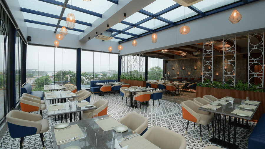 An indoor restaurant seating area featuring multiple tables, upholstered chairs, and a glass-panelled ceiling at Awesome Palace, Guwahati Airport.