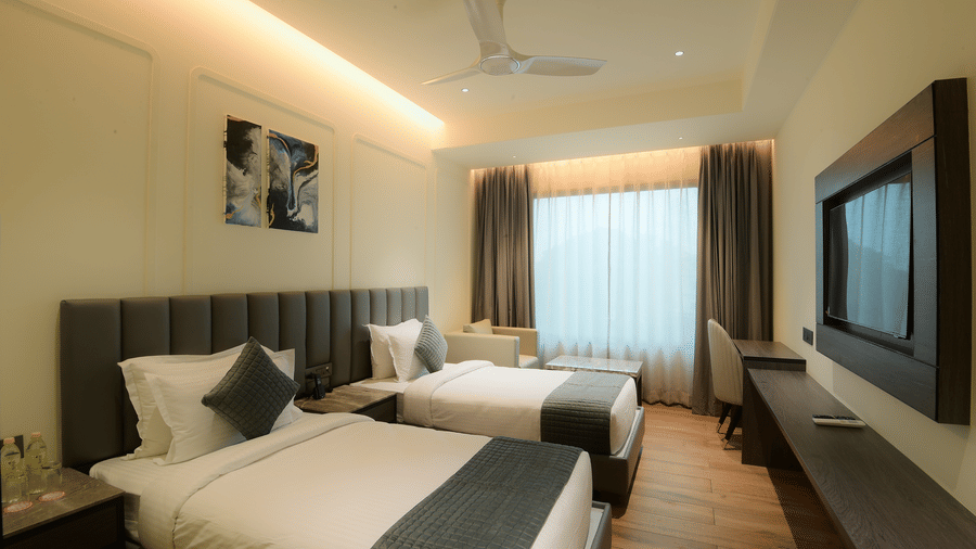 A bedroom featuring twin beds, a wall mounted television, and a desk at Awesome Palace, Guwahati Airport.
