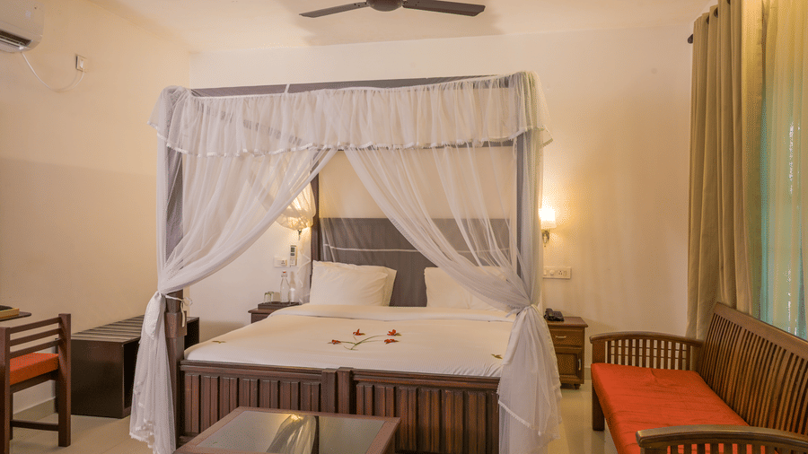 A traditional guest suite with a large canopy bed and wooden seating at Ayur On The Beach Nattika.