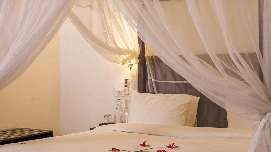 A 4-poster bed at Ayur On The Beach Nattika decorated with delicate flower petals on crisp linens.
