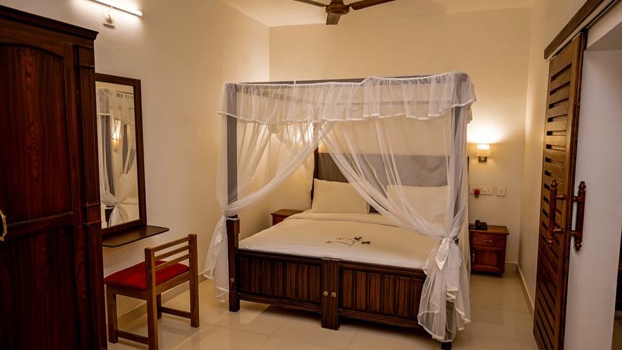 A spacious bedroom featuring a wooden 4-poster bed with a mosquito net at Ayur On The Beach Nattika.