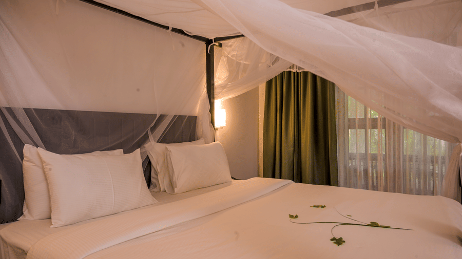A neatly made bed at Ayur On The Beach Nattika with a mosquito net and a flower petals on the linens.