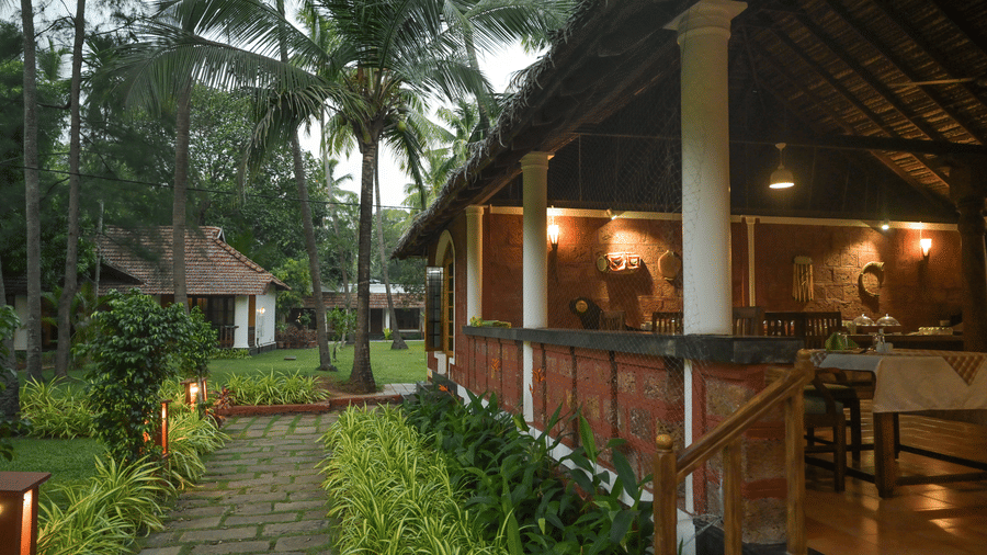 A lit garden path leading to a traditional open-air pavilion at Ayur On The Beach Nattika during twilight.