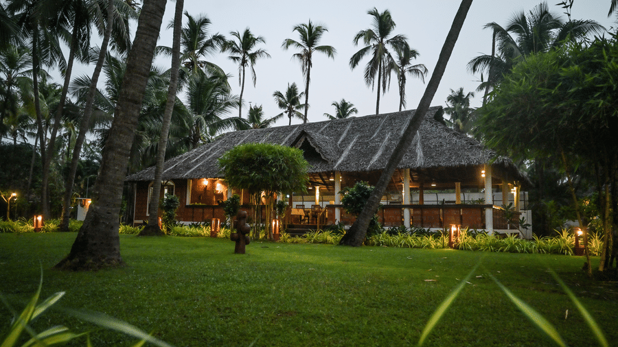 The lush green grounds of Ayur On The Beach Nattika with a traditional villa in the background.