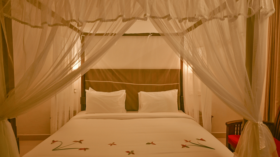 A close up of a four posted bed with a net and side lamps inside the villa at Ayur On The Beach Nattika.