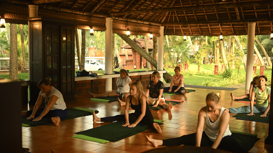 A group of people sitting on a yoga mat and practicing yoga indoors at Ayur On The Beach Nattika.