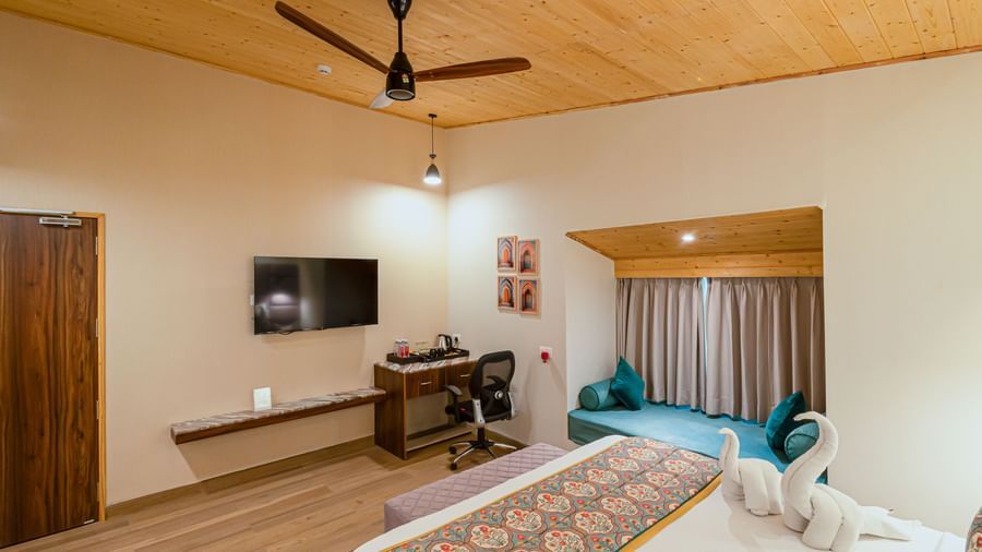 A room with a desk, television, patterned bedspread, and wooden ceiling at Bamboo Saa Resort & Spa, Udaipur.