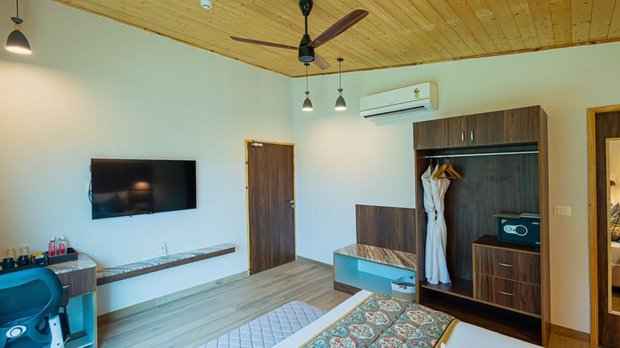 A bedroom with a mounted television, a safe, a luggage rack, and modern interior at Bamboo Saa Resort & Spa, Udaipur.