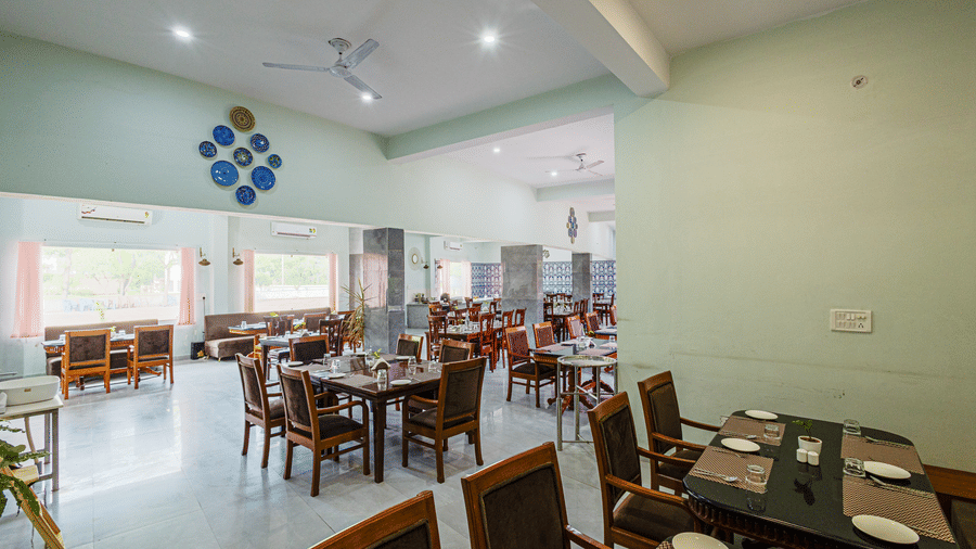 Bamboo Saa Sunrise Wedding & Wellness Resort, Jaipur dining area with multiple wooden tables and chairs, place settings, and large windows.