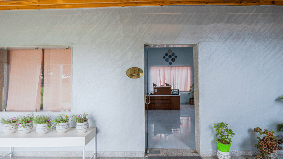 Bamboo Saa Sunrise Wedding & Wellness Resort, Jaipur exterior showing a white wall, doorway, bench, and potted plants on either side.