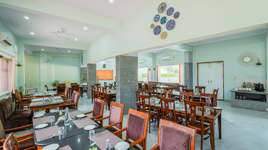Bamboo Saa Sunrise Wedding & Wellness Resort, Jaipur dining area with square tables, chairs, plates set on tables, and wall decoration.