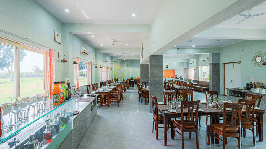 Bamboo Saa Sunrise Wedding & Wellness Resort, Jaipur long dining area with tables, chairs, glass partition, and windows along the wall.