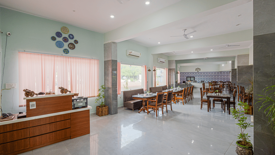 Bamboo Saa Sunrise Wedding & Wellness Resort, Jaipur reception and dining area with tables, chairs, desk, and large windows with curtains.