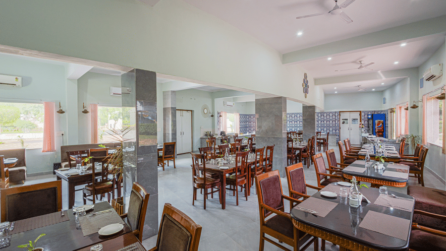 Bamboo Saa Sunrise Wedding & Wellness Resort, Jaipur spacious dining hall with multiple tables and chairs arranged in rows and mirrors on walls.