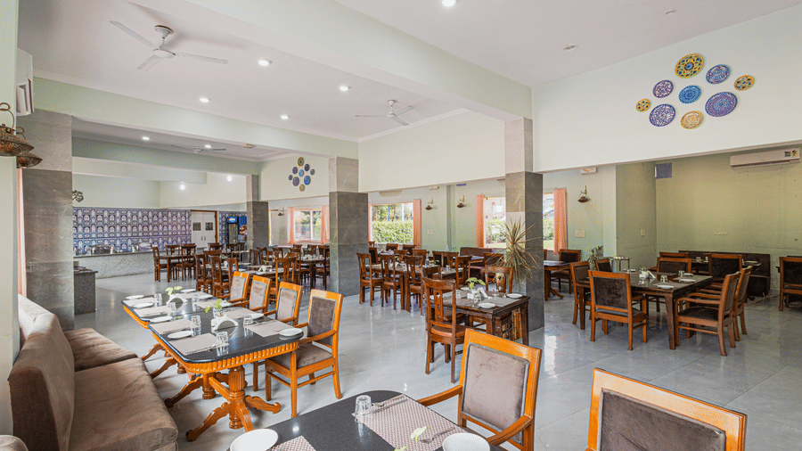 Bamboo Saa Sunrise Wedding & Wellness Resort, Jaipur large dining space with tables, chairs, place settings, and wall-mounted decorative element.