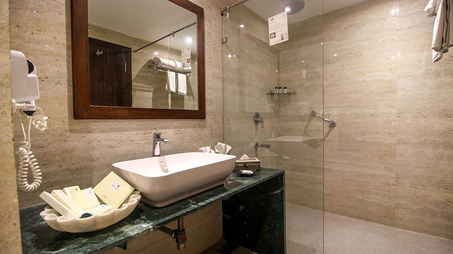 A modern bathroom with a glass shower, a sink on a dark counter, and a large mirror. - Bamboo Saa Resort & Spa, Udaipur