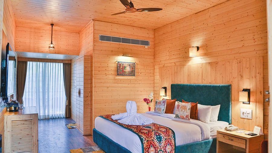 A cosy bedroom with wooden paneling, curtains, a plush bed and warm lighting. - Bamboo Saa Resort & Spa, Udaipur