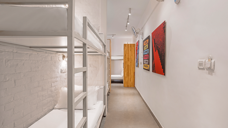 An image of dorms with the bunker beds, in bedzzz Varanasi, with few painting hanging on the wall, lighting and cupboard in it. 