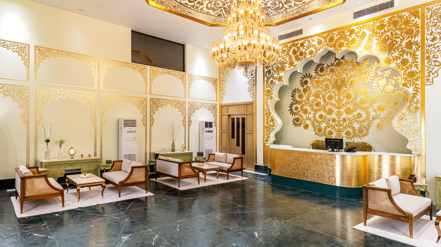 A reception area of a hotel with seating area, a reception desk, and a decorative wall featuring a chandelier and artistic patterns.