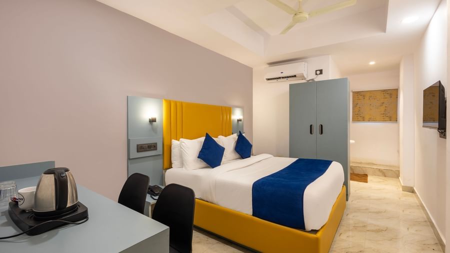 Side view of a Deluxe Room with a bed, blue and white bedding, a yellow headboard, and a desk area - Beestay Hotels Financial District, Hyderabad 