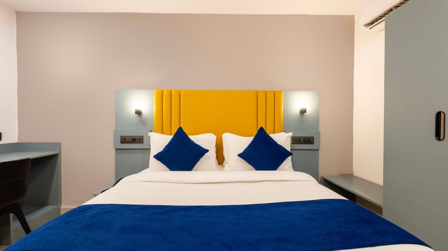 Close up of a Deluxe Room with a bed, blue and white bedding, a yellow headboard, and a desk area - Beestay Hotels Financial District, Hyderabad 