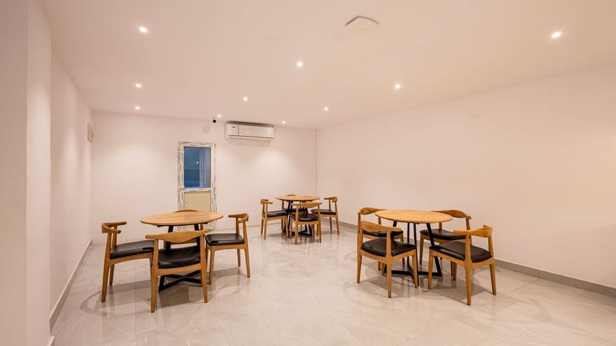 A brightly lit, minimalist dining or common area with several wooden tables and chairs arranged on a light-colored floor - Beestay Hotels Financial District, Hyderabad 
