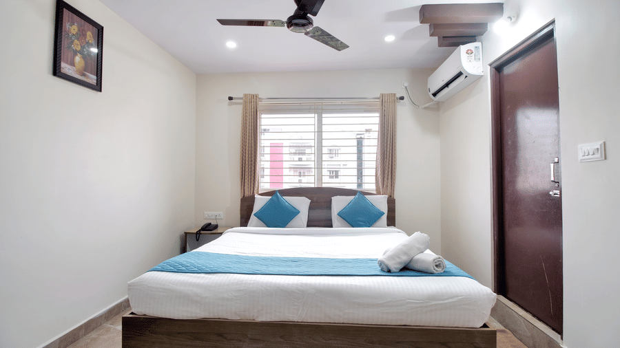 Well-lit hotel interior with a large bed, neutral tiled flooring, and a flat-screen TV, offering a tidy and welcoming atmosphere at beestay Hotels, MVP Colony, Vizag.