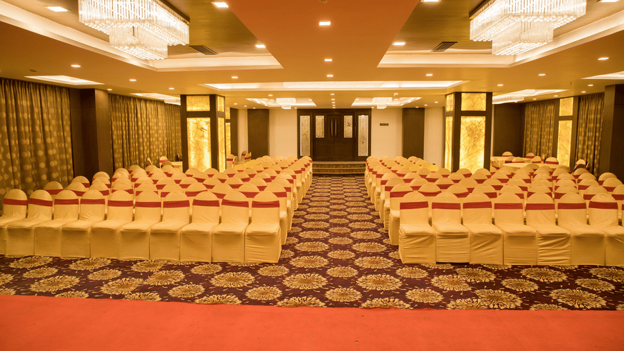 A banquet hall at Benzz Park Chennai arranged with numerous chairs in rows, featuring a patterned carpet and warm lighting.