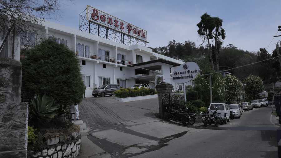The Benzz Park hotel building exterior on a hillside road, surrounded by trees and vehicles.