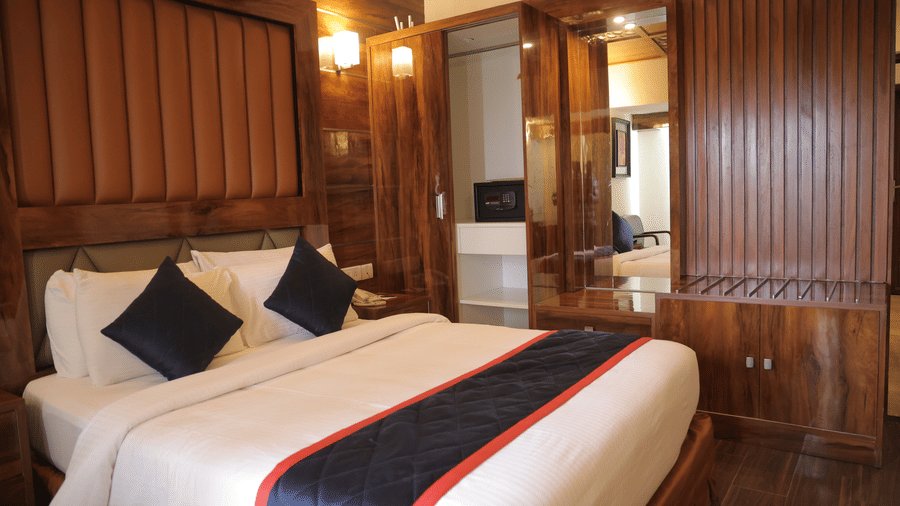 A spacious hotel suite with a large double bed, wooden panelling, and mirrored wardrobe doors - Benzz Park, Kodaikanal