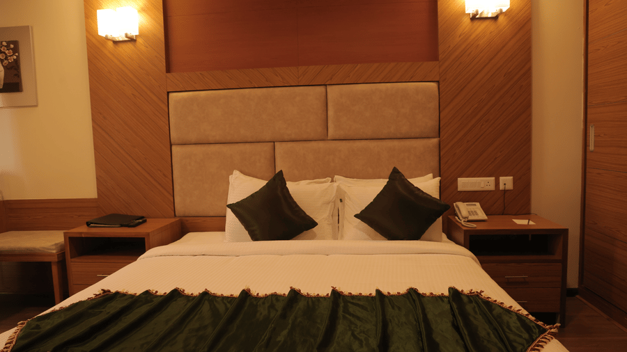 A well-appointed hotel room with a large bed, headboard, bedside tables, and a green bed runner - Benzz Park, Kodaikanal