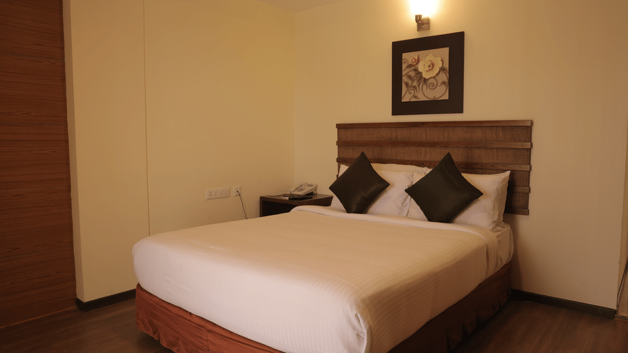 A simple, inviting hotel room showcasing a double bed with dark pillows and a wooden frame - Benzz Park, Kodaikanal