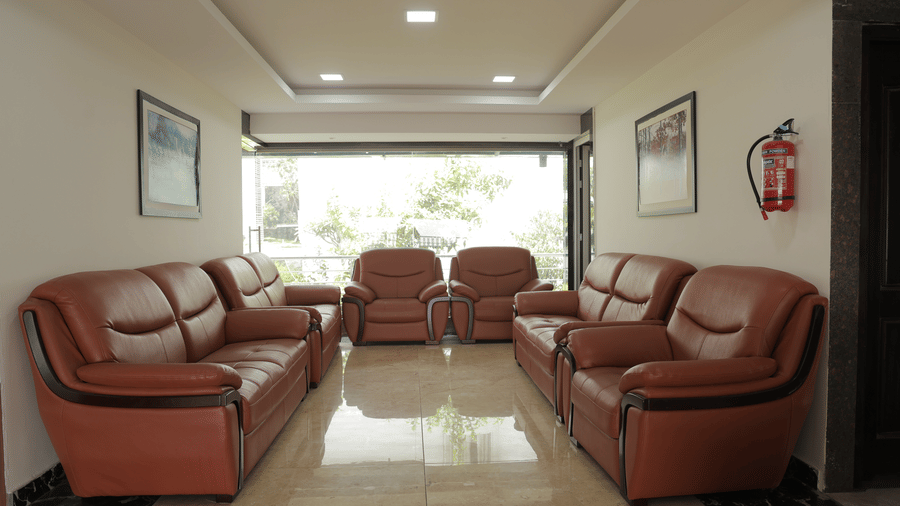 A hotel lobby with two sets of brown sofas, polished tiled floor, and large windows - Benzz Park, Kodaikanal