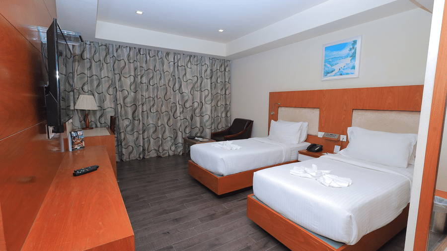 Twin room at Benzz Park, Vellore. Two single beds with white linens, towel swans, wood floor, and wooden furniture including a desk and TV stand.