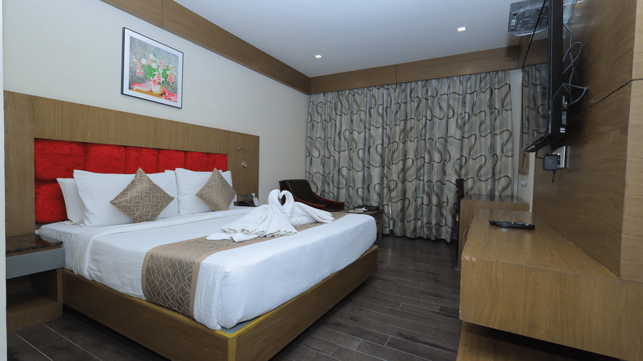 A room at Benzz Park, Vellore. Queen bed with towel swans, red headboard, wood floor, and mounted TV.