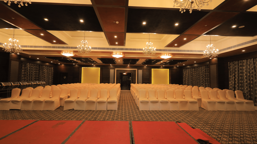Front view of the Rolse Royse hall at Benzz Park, Vellore, featuring elegant chandeliers hanging from the ceiling along with a red-carpeted stage in the foreground.