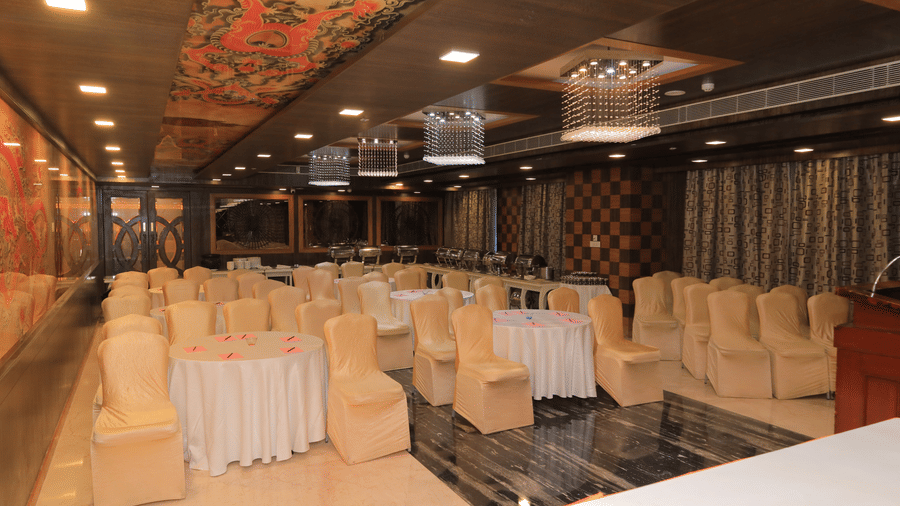 Corner view of the Bentley hall at Benzz Park, Vellore, featuring chairs surrounding round tables facing towards the stage in front of them.