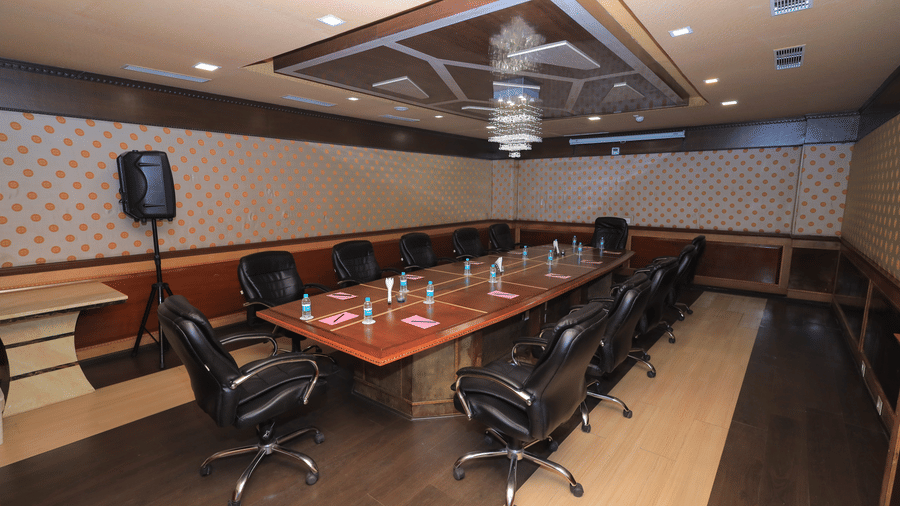 Benzz Park, Vellore Conference Room. Long wooden table, black leather chairs, speaker, and gold patterned wallpaper with wood paneling.