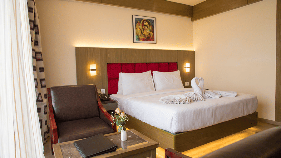 Side angle view of a double bed in a brightly lit Deluxe Room with a back lit headboard at the Benzz Park, Vellore.