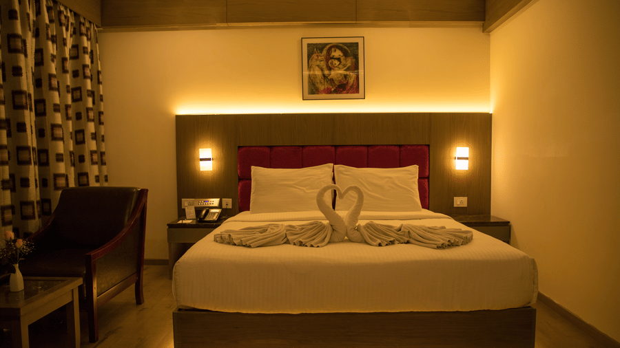A cosy Deluxe Room with warm lighting featuring a double bed alongside an armchair at the Benzz Park, Vellore.