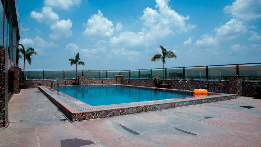 Full view of the rooftop swimming pool at the Benzz Park, Vellore, featuring a clear blue sky in the background with a few palm trees on the perimeter.