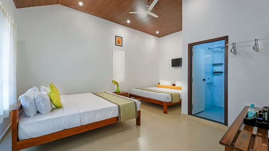 A bright and airy family room at Bhuthanakadu Retreat, featuring two comfortable beds with vibrant green and white bedding, and a ceiling fan.