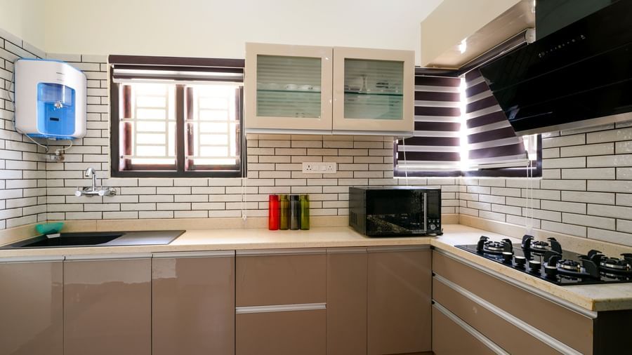 A clean, modern kitchen in the villa at Bhuthanakadu Retreat, featuring beige cabinets, white subway tile backsplash, and a built-in cooktop and microwave.