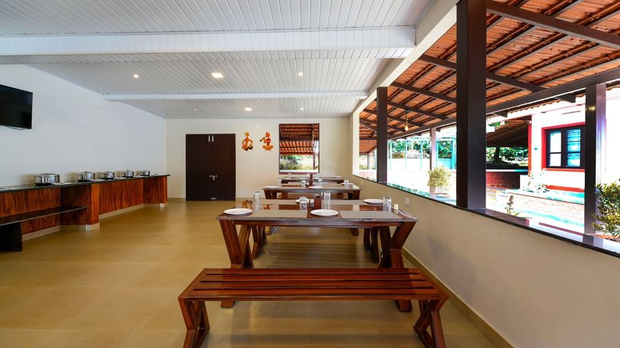 A panoramic shot of the Mane Cafe at Bhuthanakadu Retreat, emphasizing the casual, inviting atmosphere of the dining area with a long serving station and windows overlooking the outdoors.