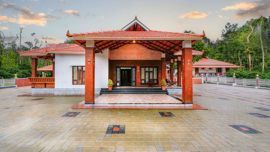A frontal shot of the traditional facade of Bhuthanakadu Retreat, showcasing the building's intricate entryway and a colorful, patterned tiled courtyard with a water fountain.