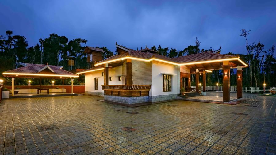 An evening shot of the main building at Bhuthanakadu Retreat, illuminated by string lights and a bright sign, with the sky transitioning from day to night.