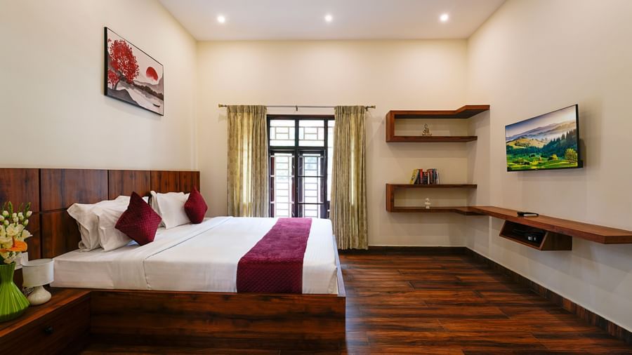 A comfortable bedroom in the villa at Bhuthanakadu Retreat, featuring a large wooden bed with a maroon and white duvet, and dark wooden furniture.