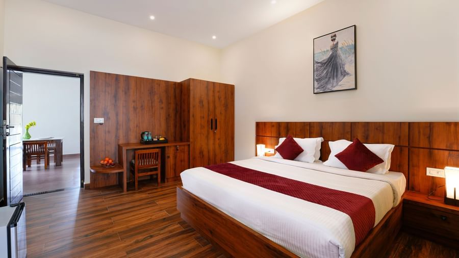 A comfortable bedroom in the villa at Bhuthanakadu Retreat, featuring a large wooden bed with a maroon and white duvet, and dark wooden furniture.