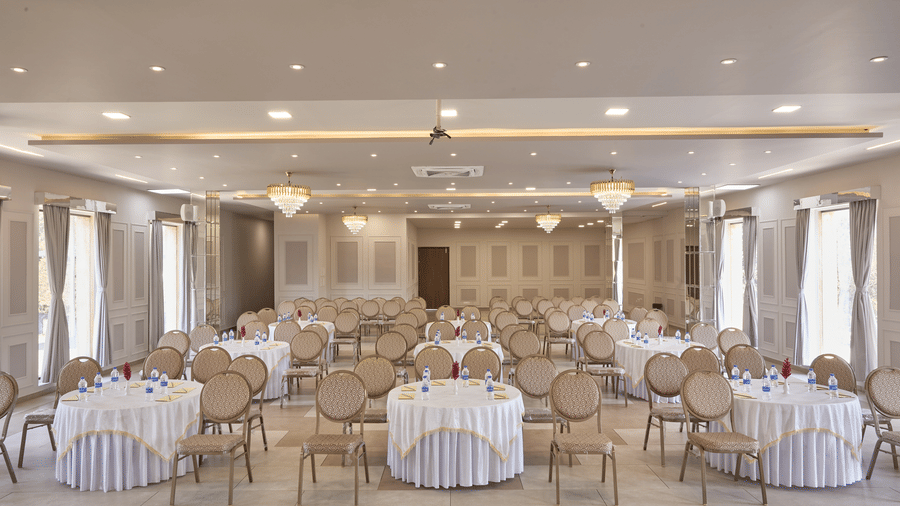 Interior of a brightly lit hotel ballroom set up for a banquet with numerous round tables and gold chairs for a formal event at Bindiga Peak Resorts.