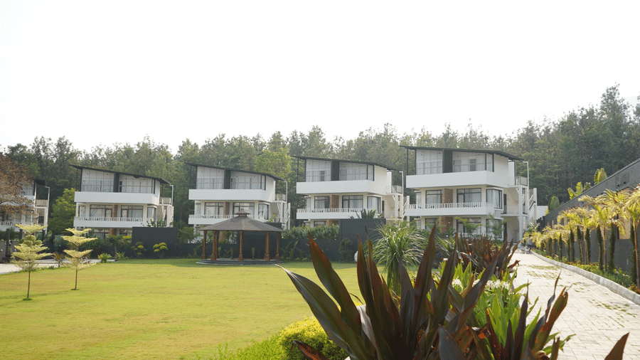 Contemporary white resort villas overlooking a wide, manicured green lawn, surrounded by tropical foliage under bright daylight at Bindiga Peak Resorts.